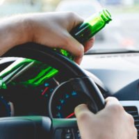 man holding a beer bottle while driving