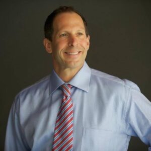 Jonathan Walner in a blue shirt and tie smiling