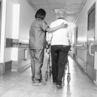 nurse helping an elderly woman walk down the hallway