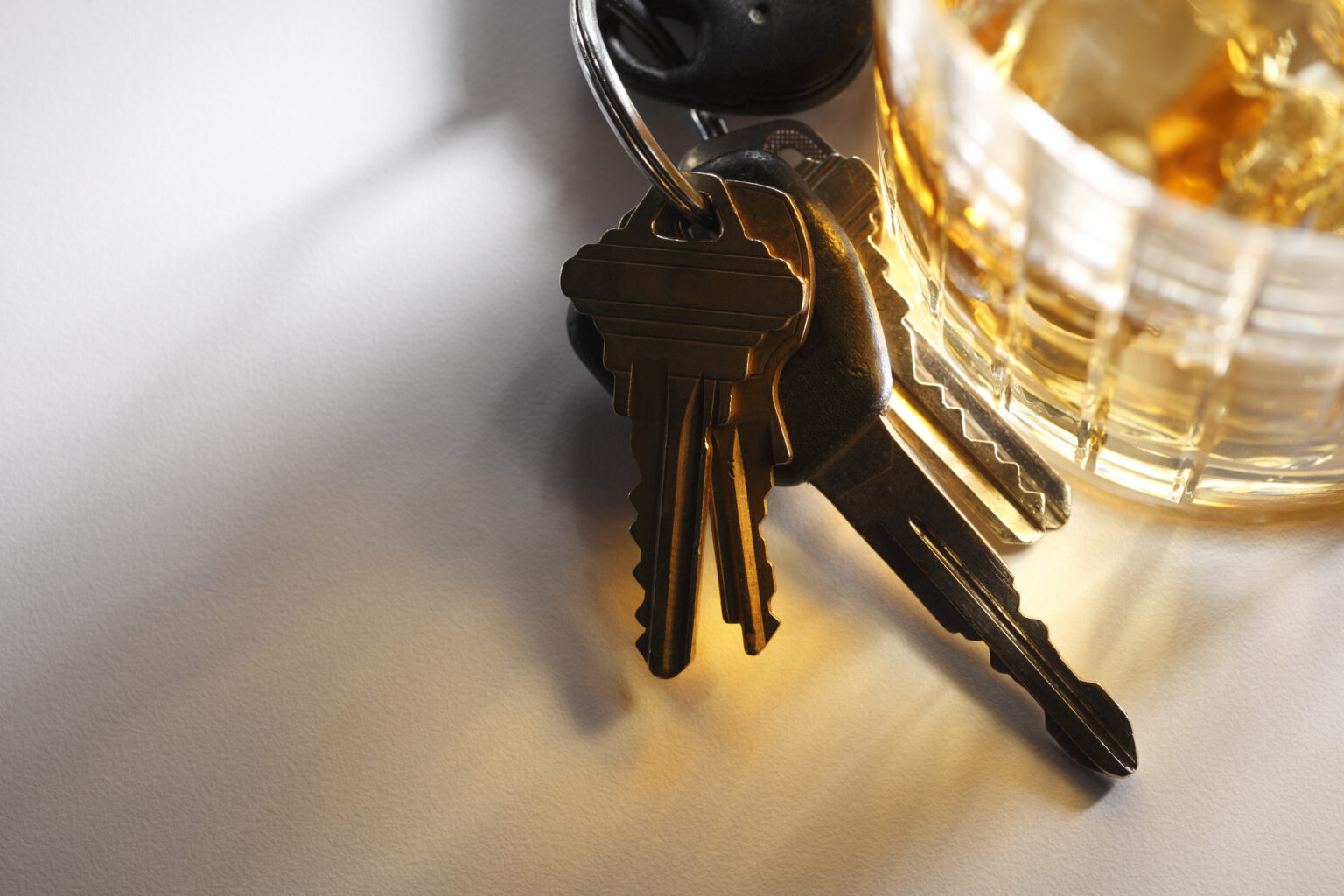 A set of keys resting next to a glass of alcohol. The concept addresses the issue of drinking and driving. A strong directional light streams through the glass and plays out across