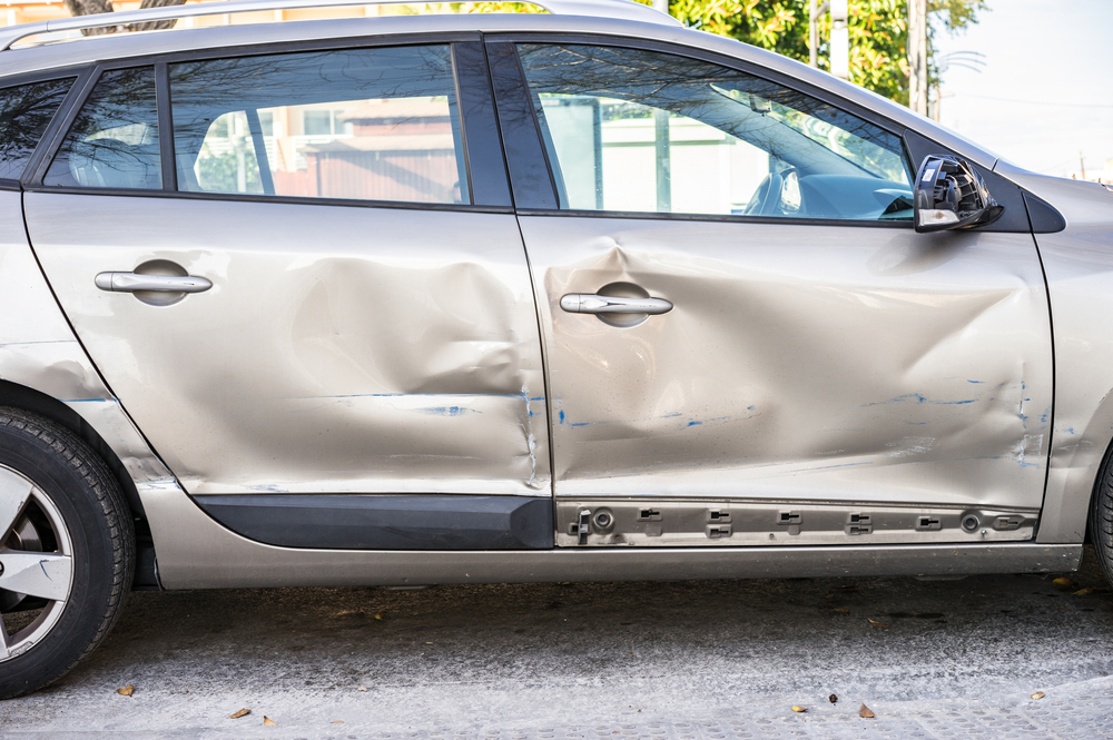 Close-up of deep scrape and dent on car door after sideswipe, showing complex damage beyond surface level.