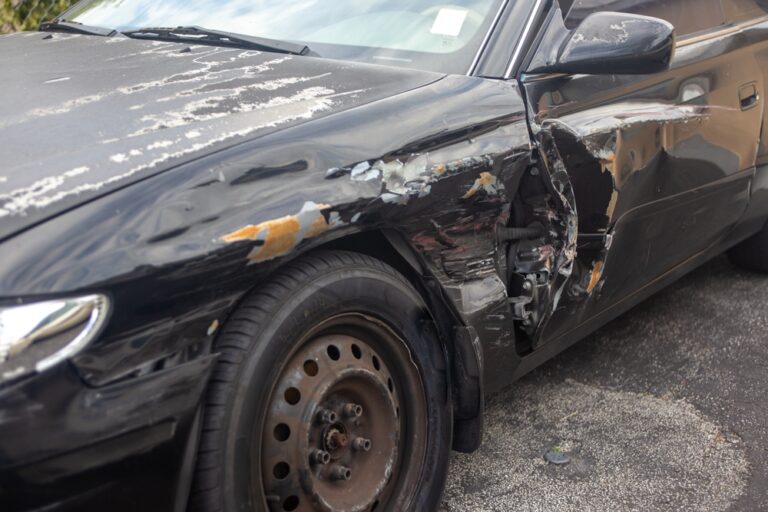 Two cars with side damage on busy street, drivers exchange information after a sideswipe collision.