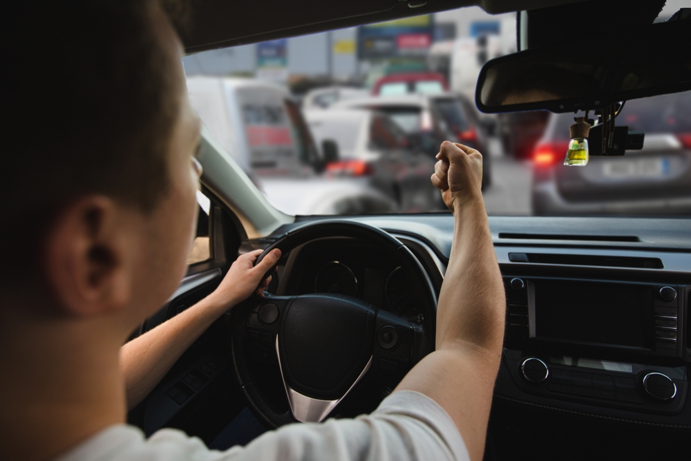 Angry driver yells and gestures aggressively through car window, showing dangerous road rage behavior.

