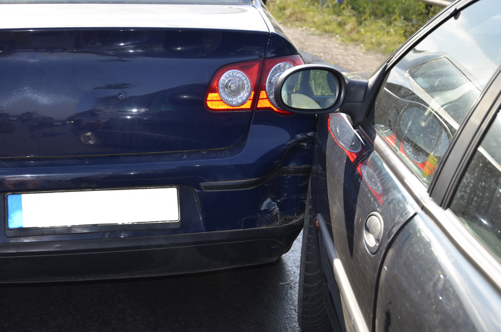 Damaged car after being sideswiped in traffic, showing dented door and scraped paint on busy road.