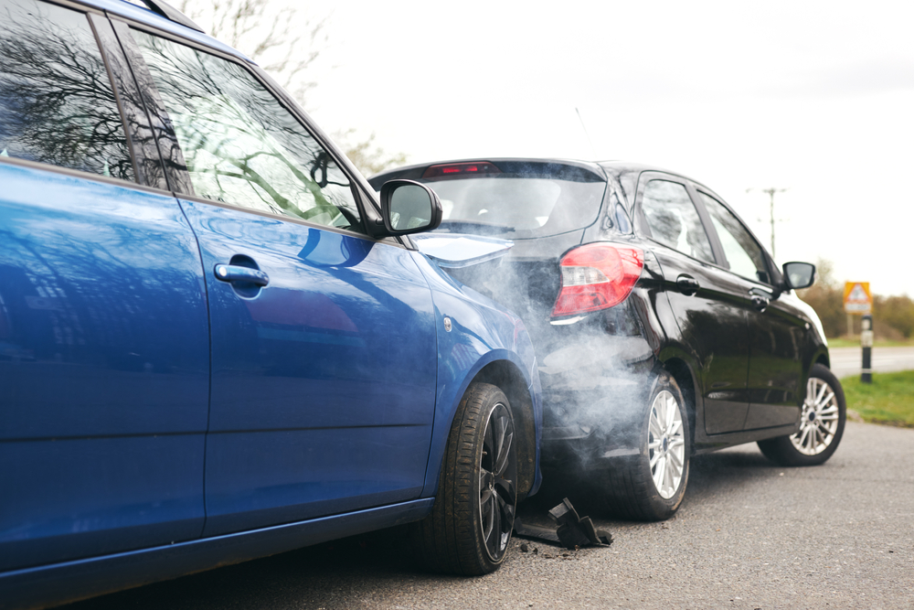 Two cars after rear-end crash, rear car damaged and driver exchanges insurance info with front driver.