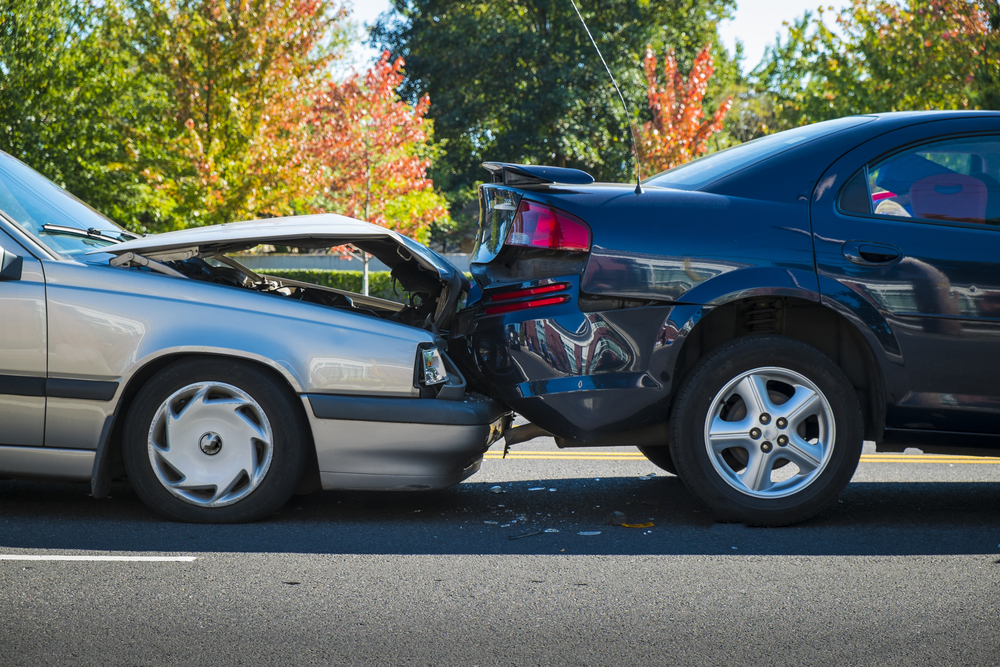 Tailgating car crashes into vehicle ahead at stoplight, showing common cause of rear-end collisions.