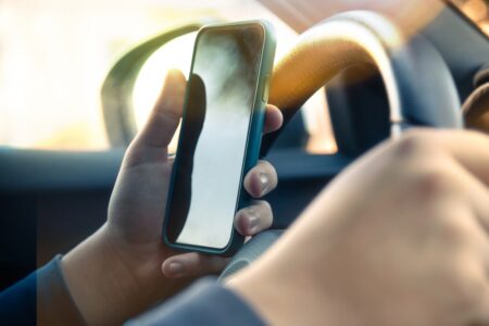 close-up phone of a person driving and using a cell phone