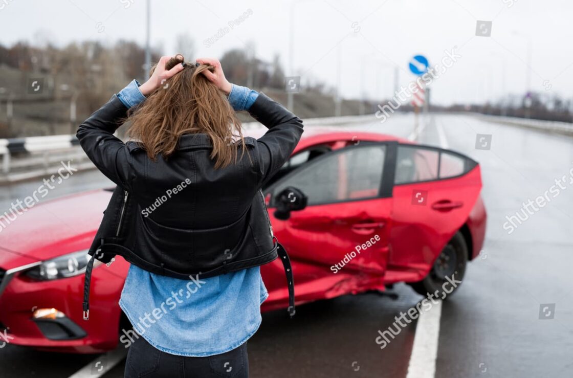 Woman stands by damaged car after sideswipe accident, calling for help—highlighting hidden damage and insurance complexities.