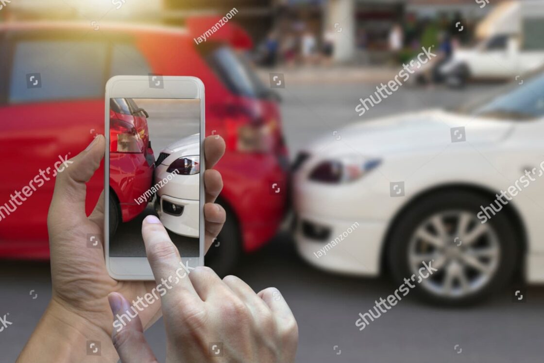 Close-up of hand taking photo of car crash with smartphone, documenting damage for insurance claim and evidence gathering.