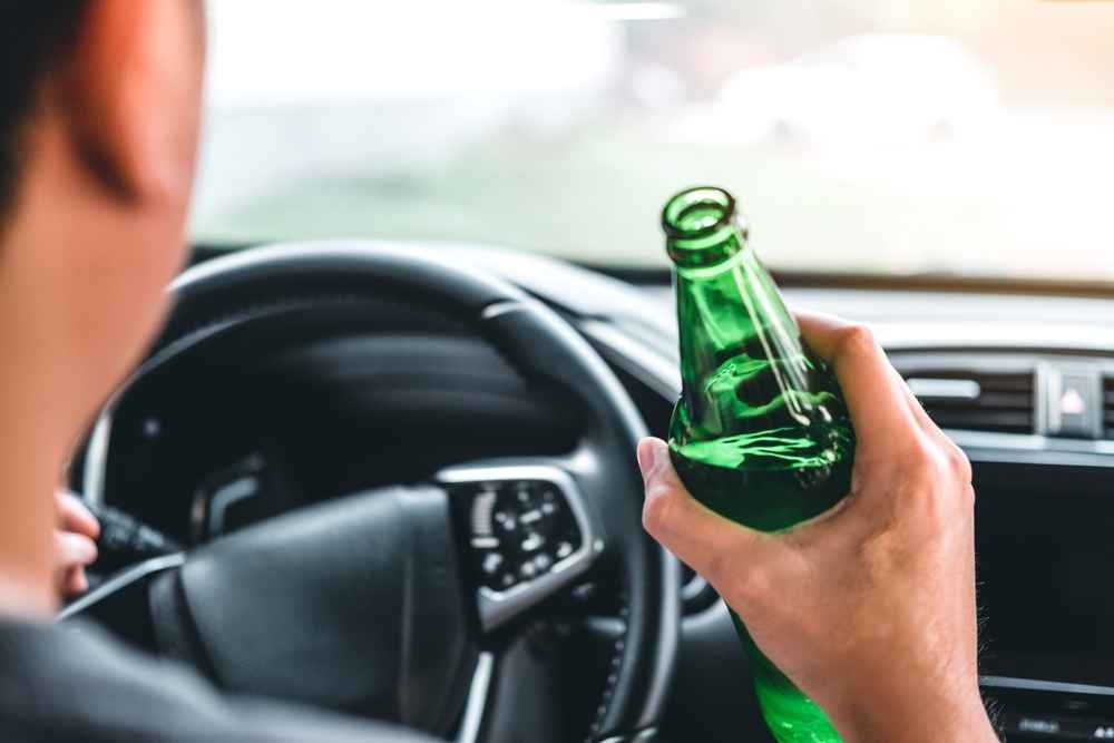 Drunk man driving a car on the road holding bottle beer Dangerous drunk driving concept