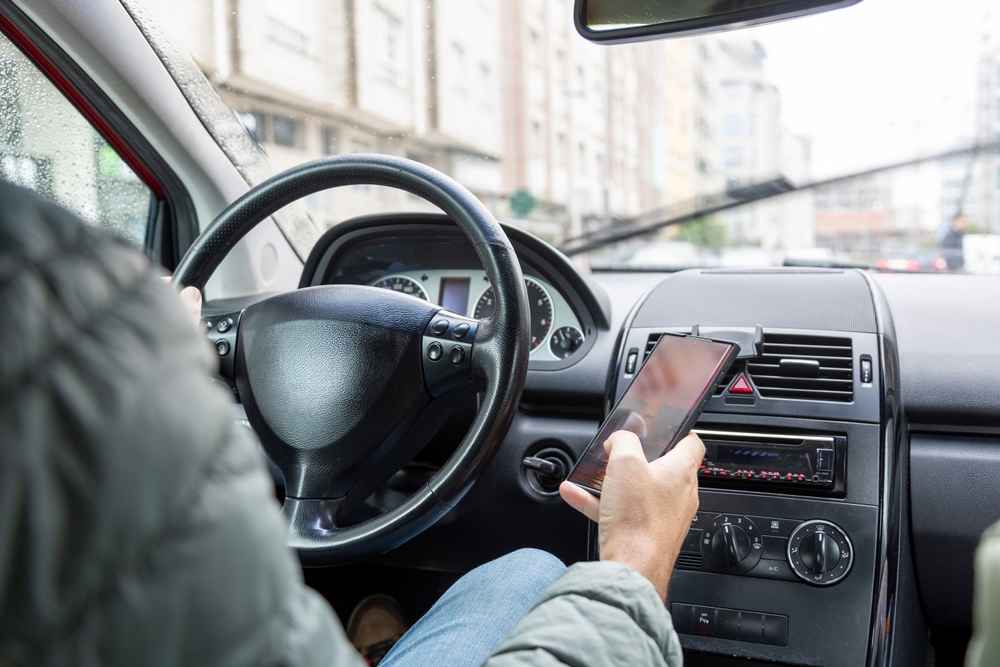 A male driver in a green jacket is dangerously using a smartphone while driving, 