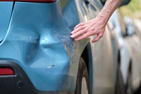 Driver hand examining dented car with damaged fender after hit and run case