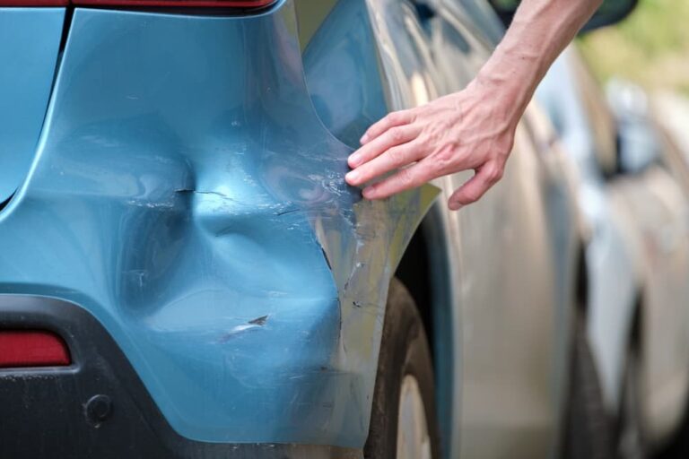 Driver hand examining dented car with damaged fender after hit and run case