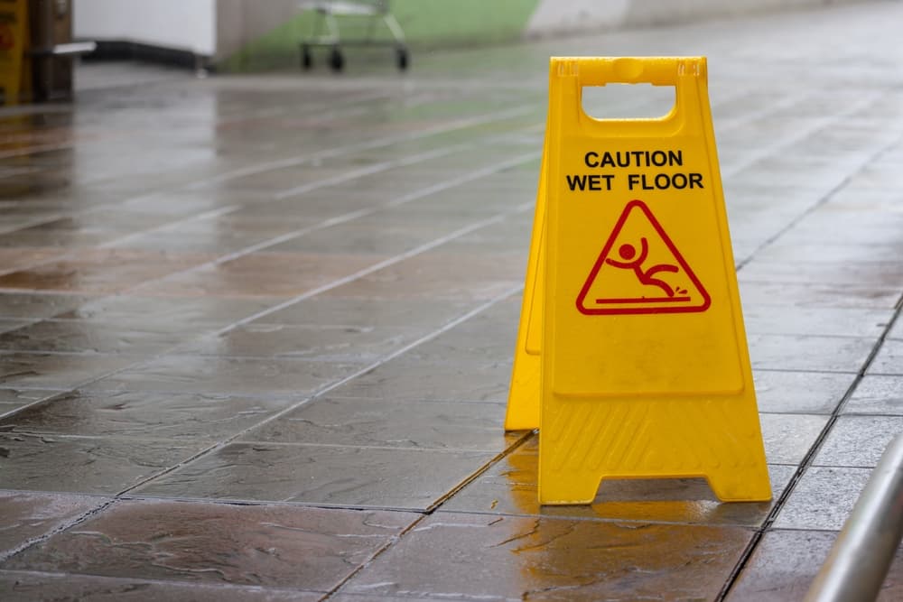 A yellow caution sign is on the ground. The sign warns people that the floor is wet.