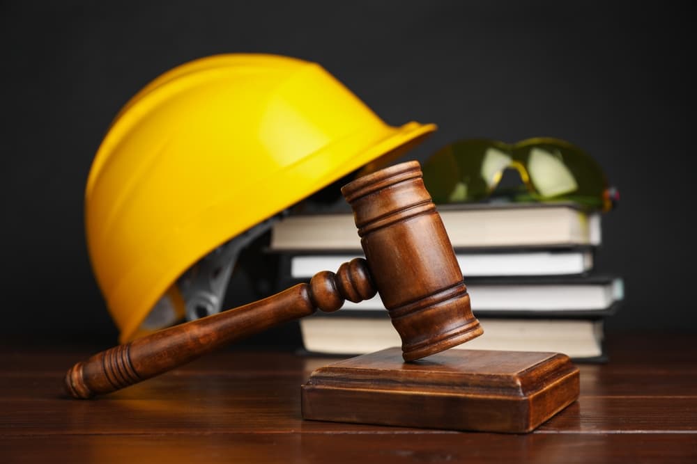 Gavel, books and construction worker's protective gear on wooden table