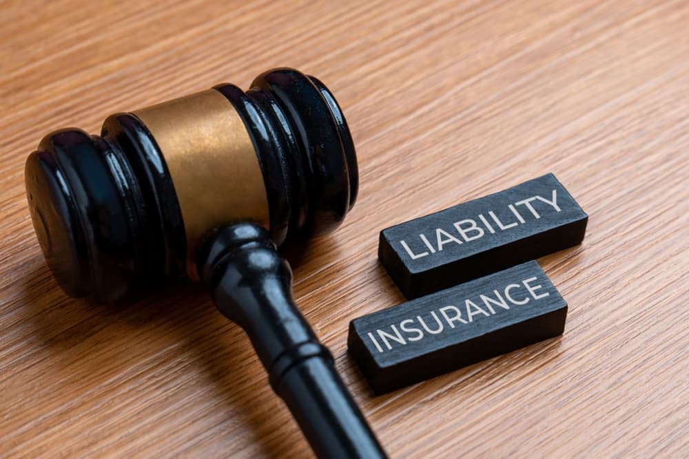 A gavel on a desk next to two stacked wooden blocks with the words LIABILITY INSURANCE. Law concept.