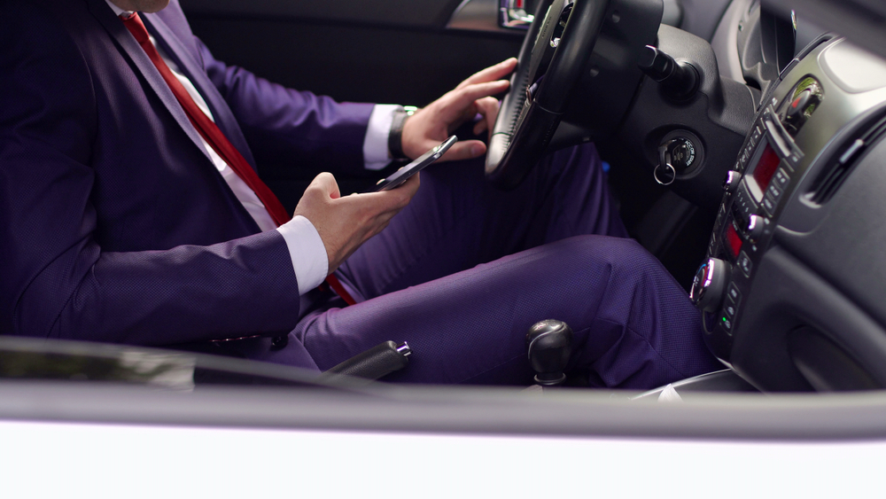 A man in a suit uses a cell phone while driving